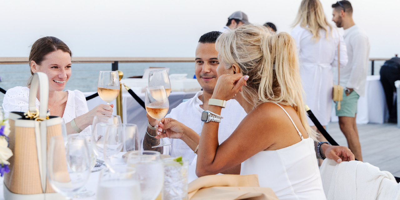A group of three dressed in white pose for a photo with the ocean in the background at Gurney's Montauk